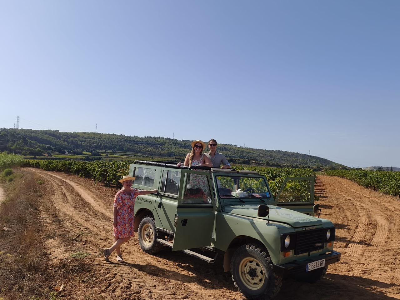 Guests posing with a vintage green Land Rover on a vineyard track in Penedès with Alexandra Kalinina, WSET Level 3 certified Cava expert and private wine guide