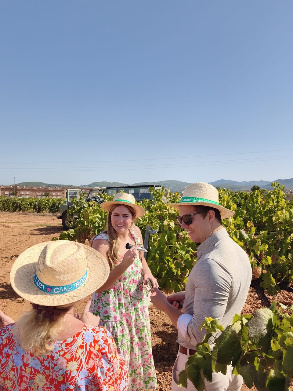 Guests in straw hats tasting wine among the vines during a Land Rover vineyard tour with Alexandra Kalinina, WSET Level 3 certified Cava expert and private wine guide