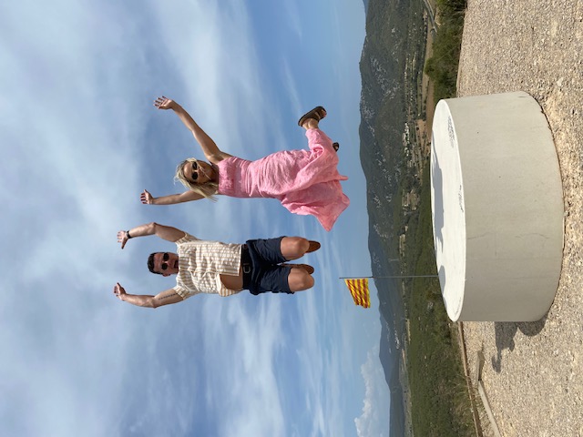 Couple jumping joyfully at a scenic viewpoint with the Catalan flag over the Penedès valley on a private wine tour with a WSET Level 3 certified Cava expert and private wine guide