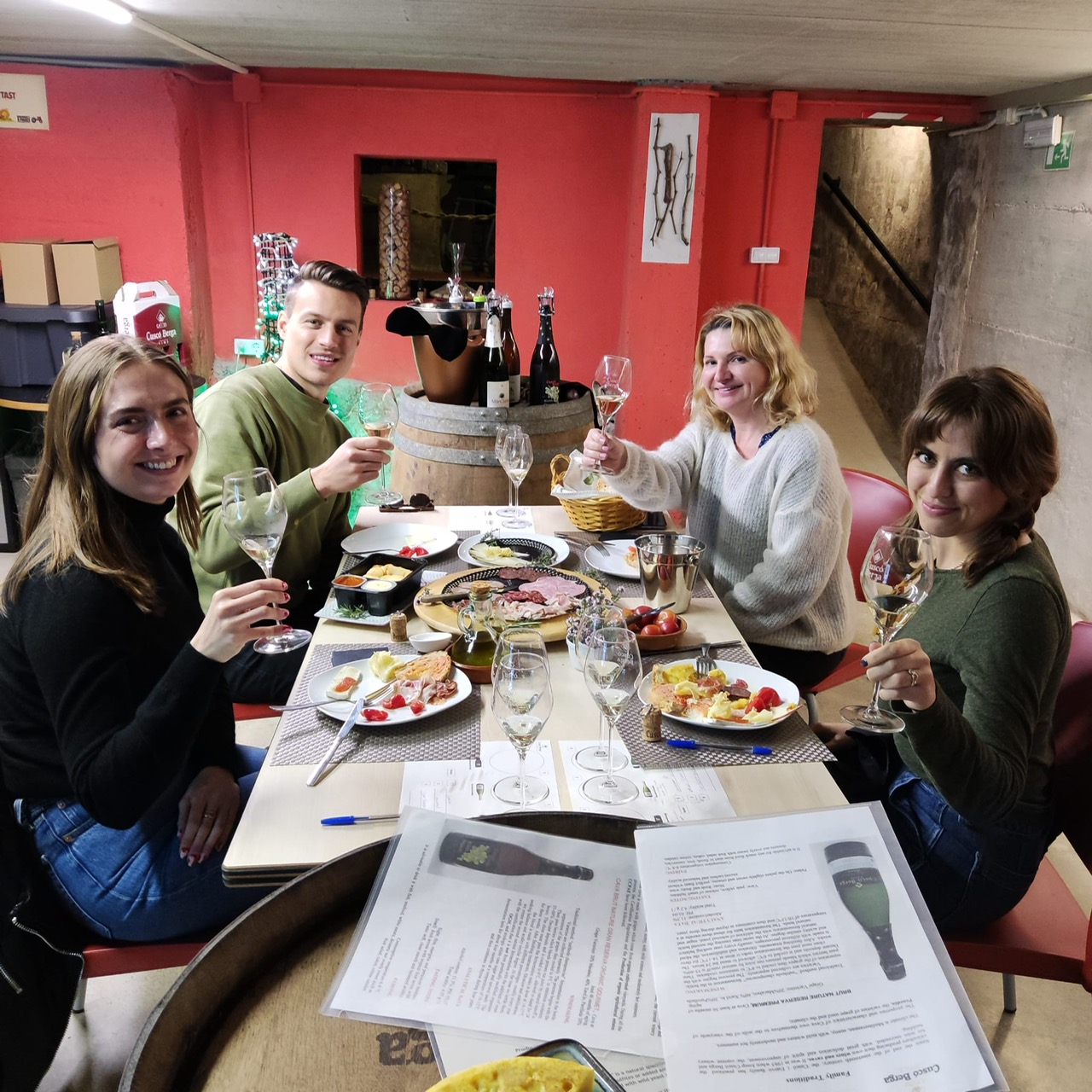 Small group toasting sparkling wine around a tasting table in a cosy winery cellar with Alexandra Kalinina, WSET Level 3 certified Cava expert and private wine guide