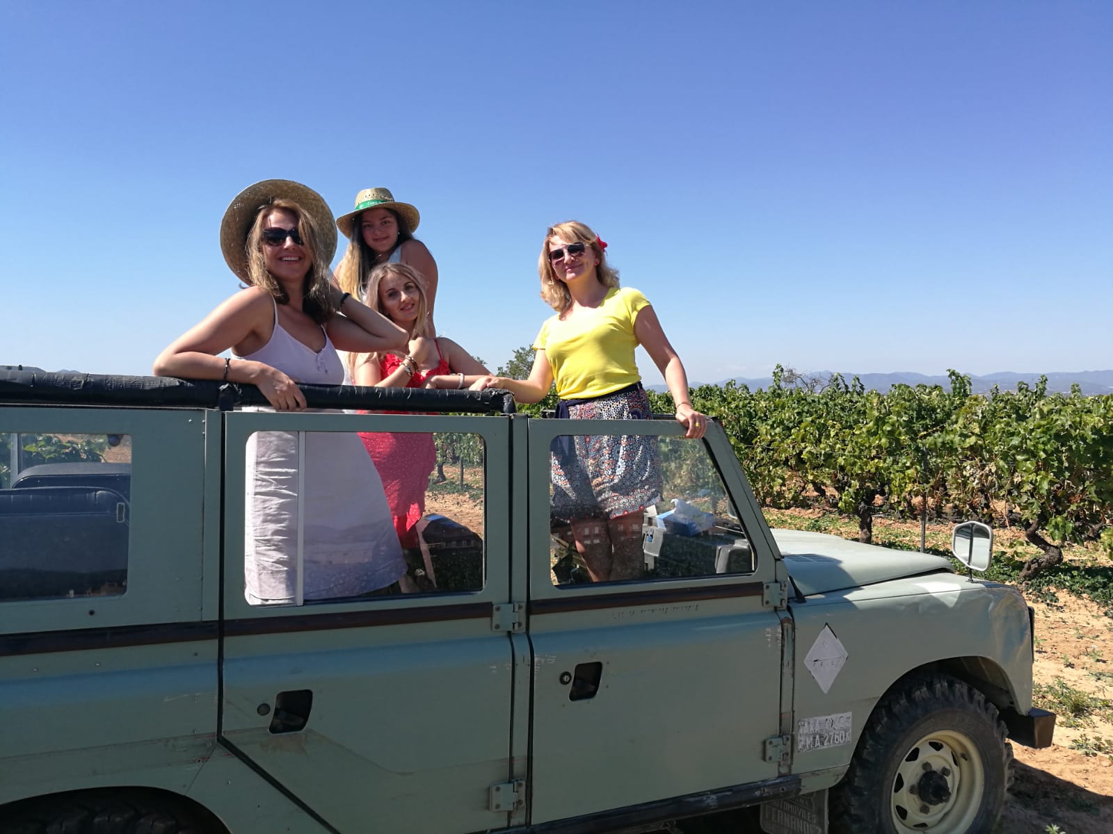 Friends posing on a vintage Land Rover among the vines