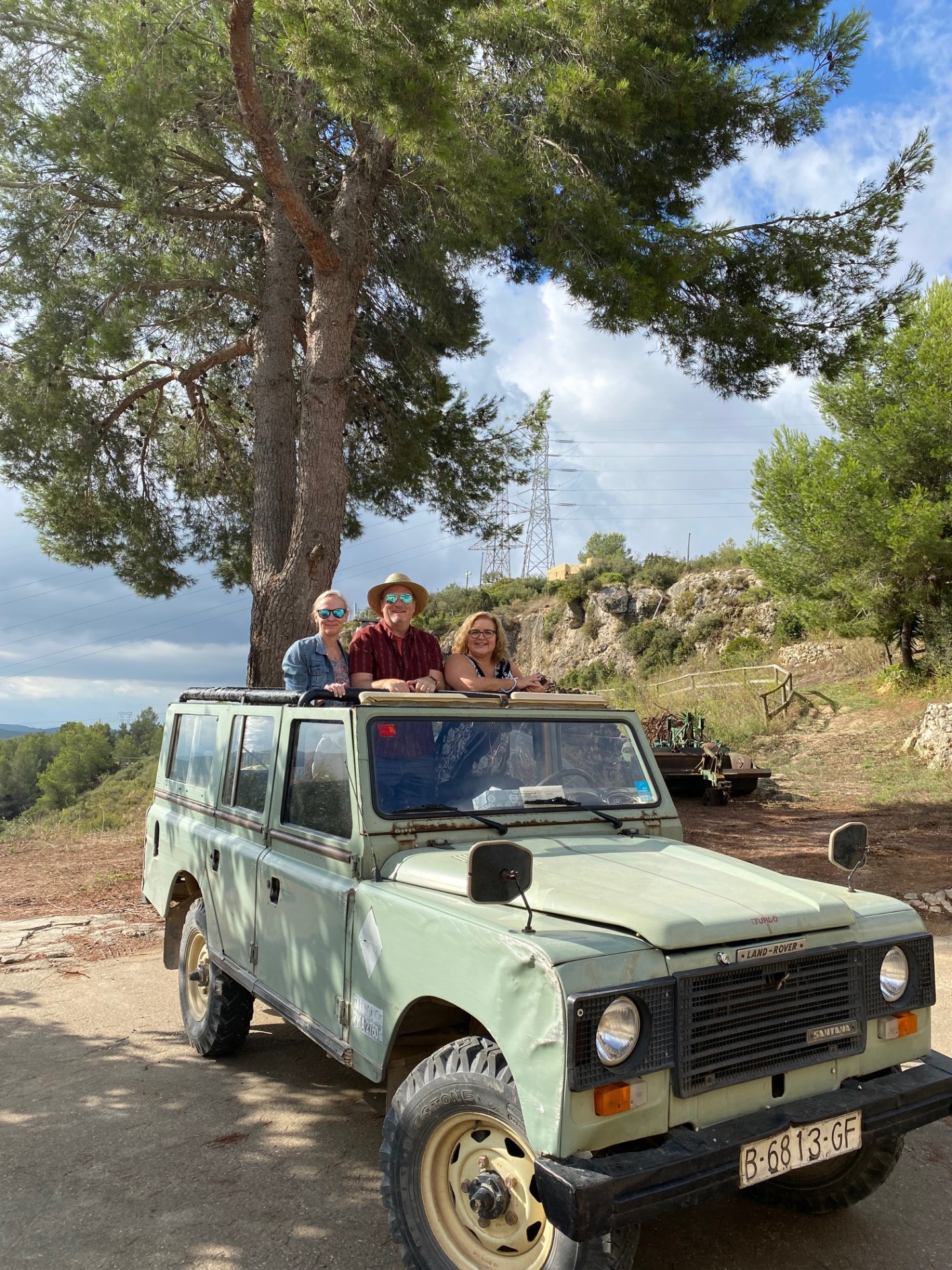 Guests posing on a vintage green Land Rover under a pine tree
